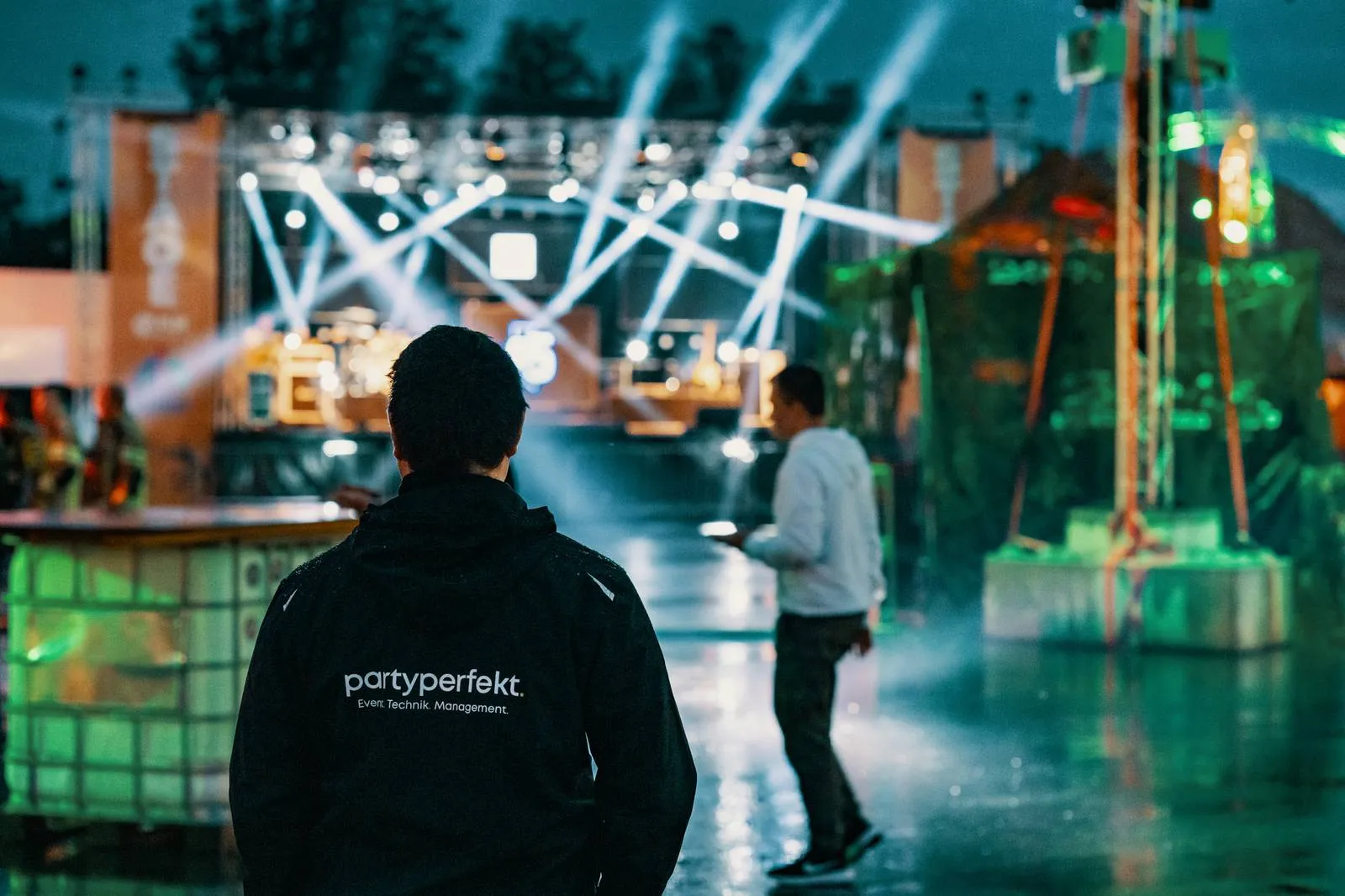 partyperfekt.-Teamjacke von hinten, Blick auf die beleuchtete Open-Air-Bühne