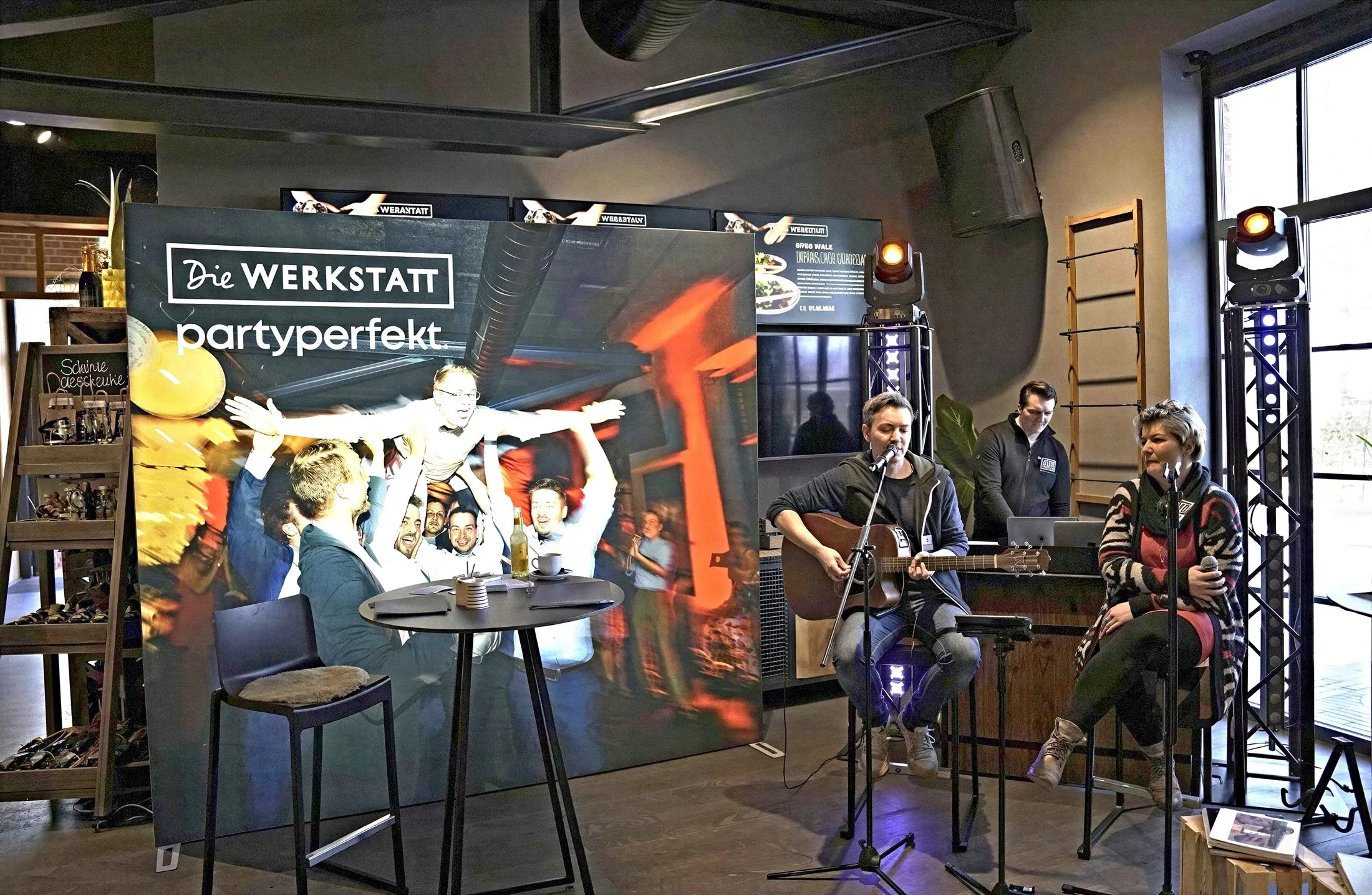 Sänger mit Gitarre und Sängerin am Mikrofon beim Auftritt, DJ-Pult im Hintergrund