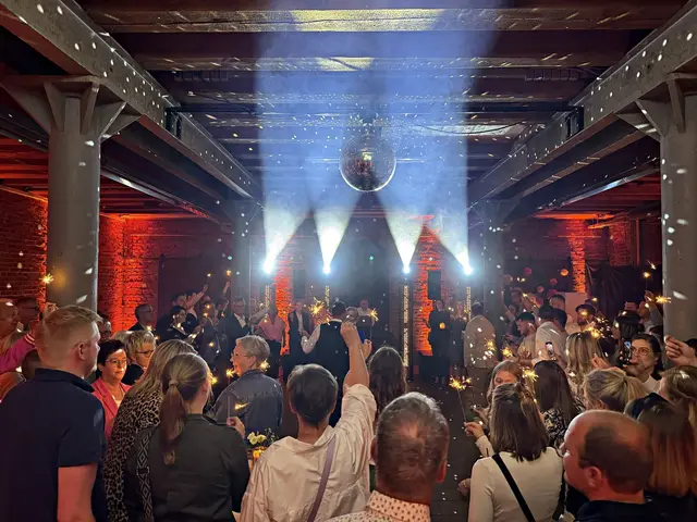 Discokugel und Lichtkegel über einer vollen Tanzfläche, Gäste mit Wunderkerzen