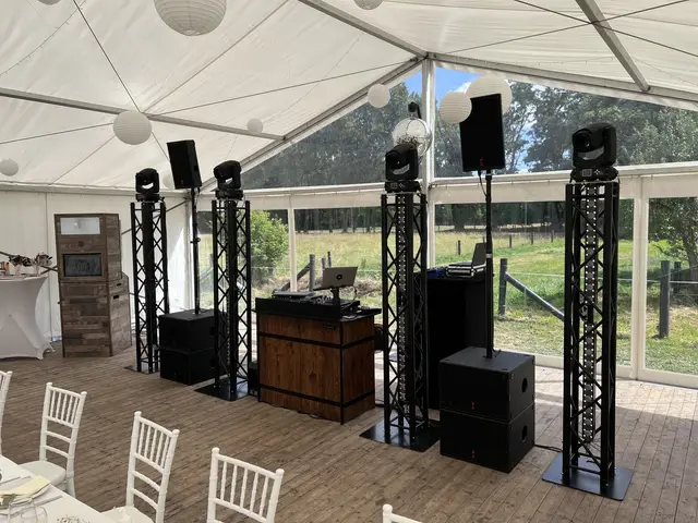 DJ-Pult mit vier Truss Tower black in einem hellen Gartenzelt, Stühle davor