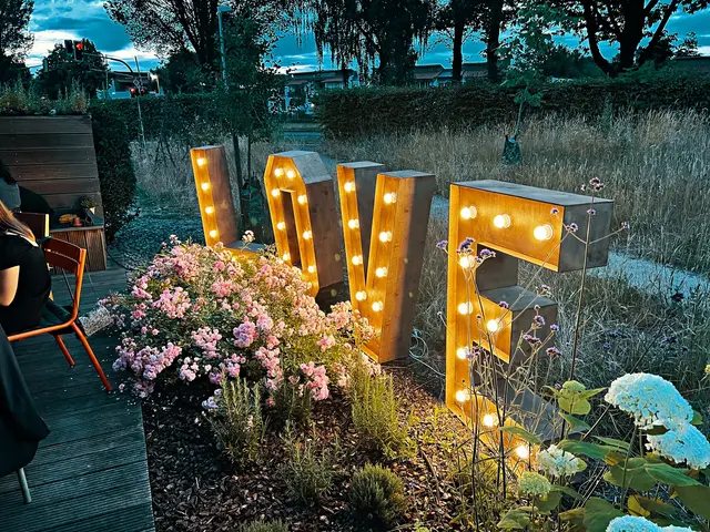 Leuchtende Love-Buchstaben zwischen Hortensien im Garten, Dämmerung