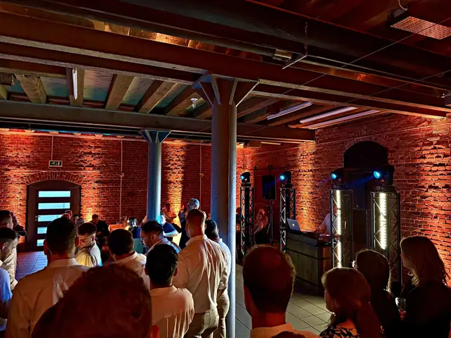 Gäste vor dem DJ-Pult in einer Backsteinhalle, blaue Lichtstrahlen über den Köpfen