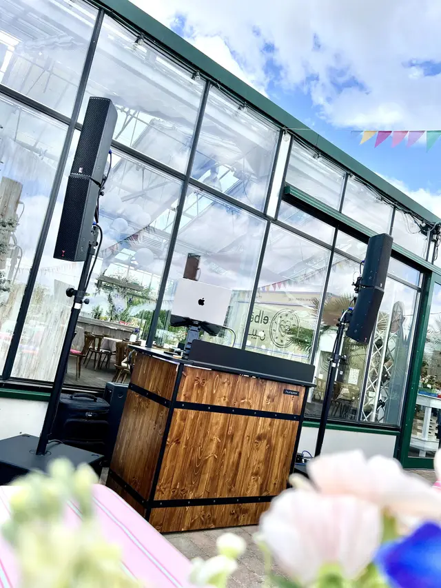 DJ-Pult im verglasten Wintergarten bei Tageslicht, bunte Wimpelkette im Hintergrund