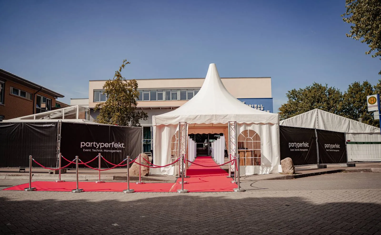 Roter Teppich mit Pagodenzelt und gebrandeten Bauzäunen bei einem Abiball