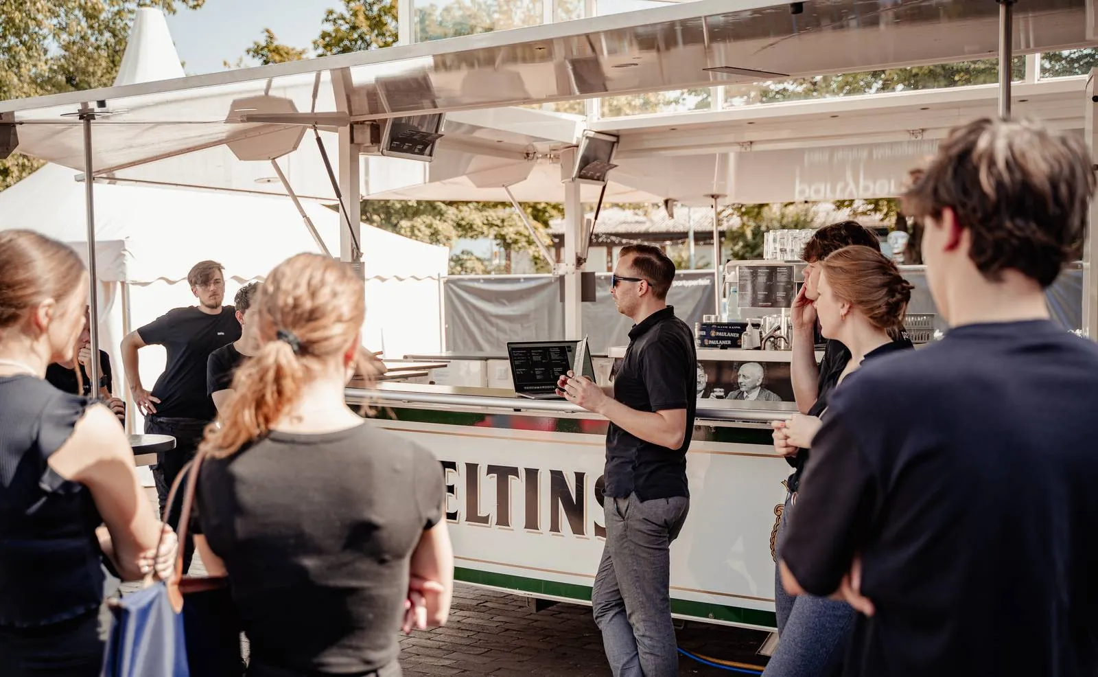 Team-Briefing vor Veranstaltungsbeginn, Einweisung des Serviceteams mit Laptop am Ausschankwagen