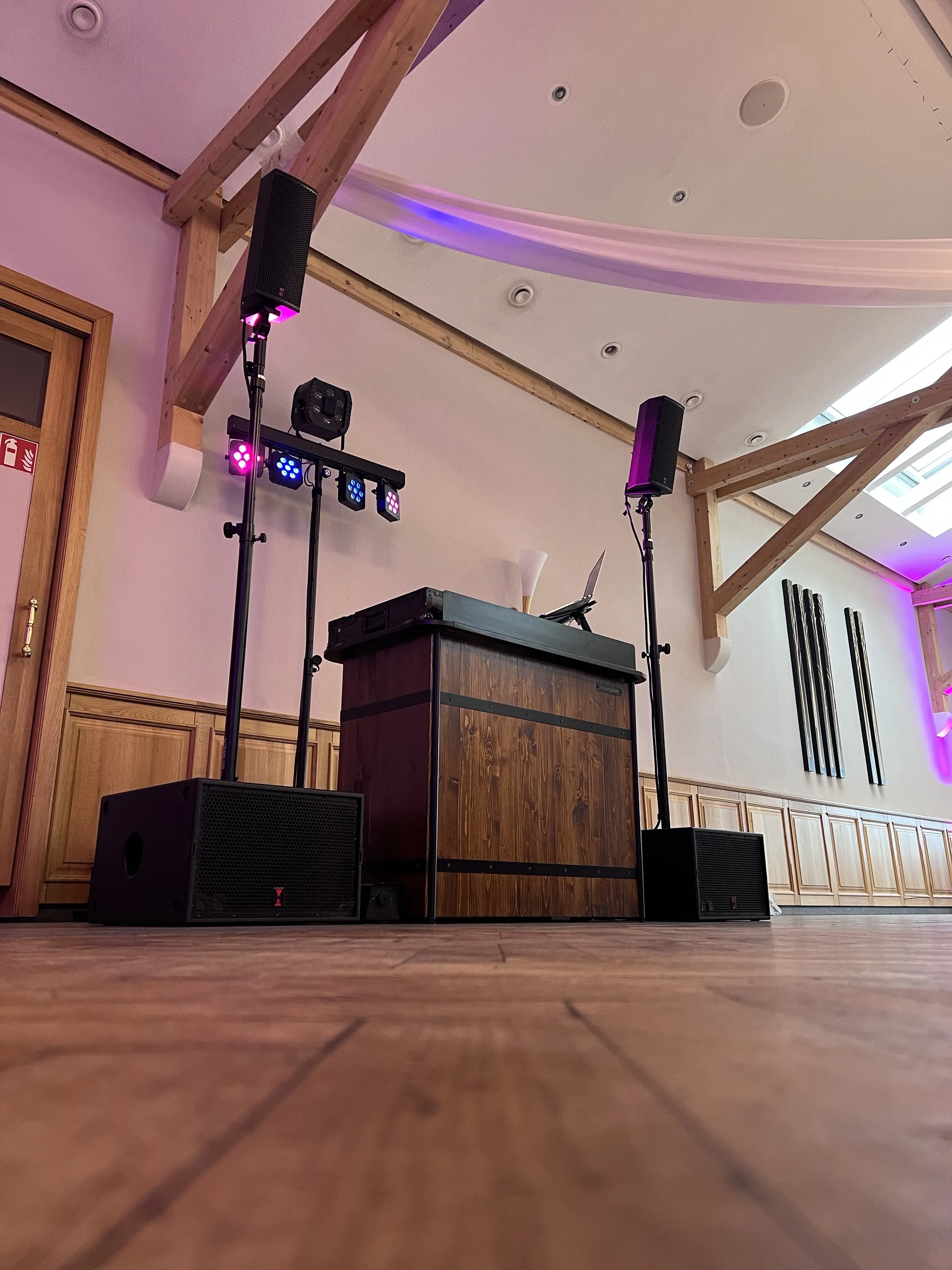 DJ-Pult mit Lautsprechern und Lichtstativen, aufgebaut in einem hellen Saal mit Holzbalkendecke